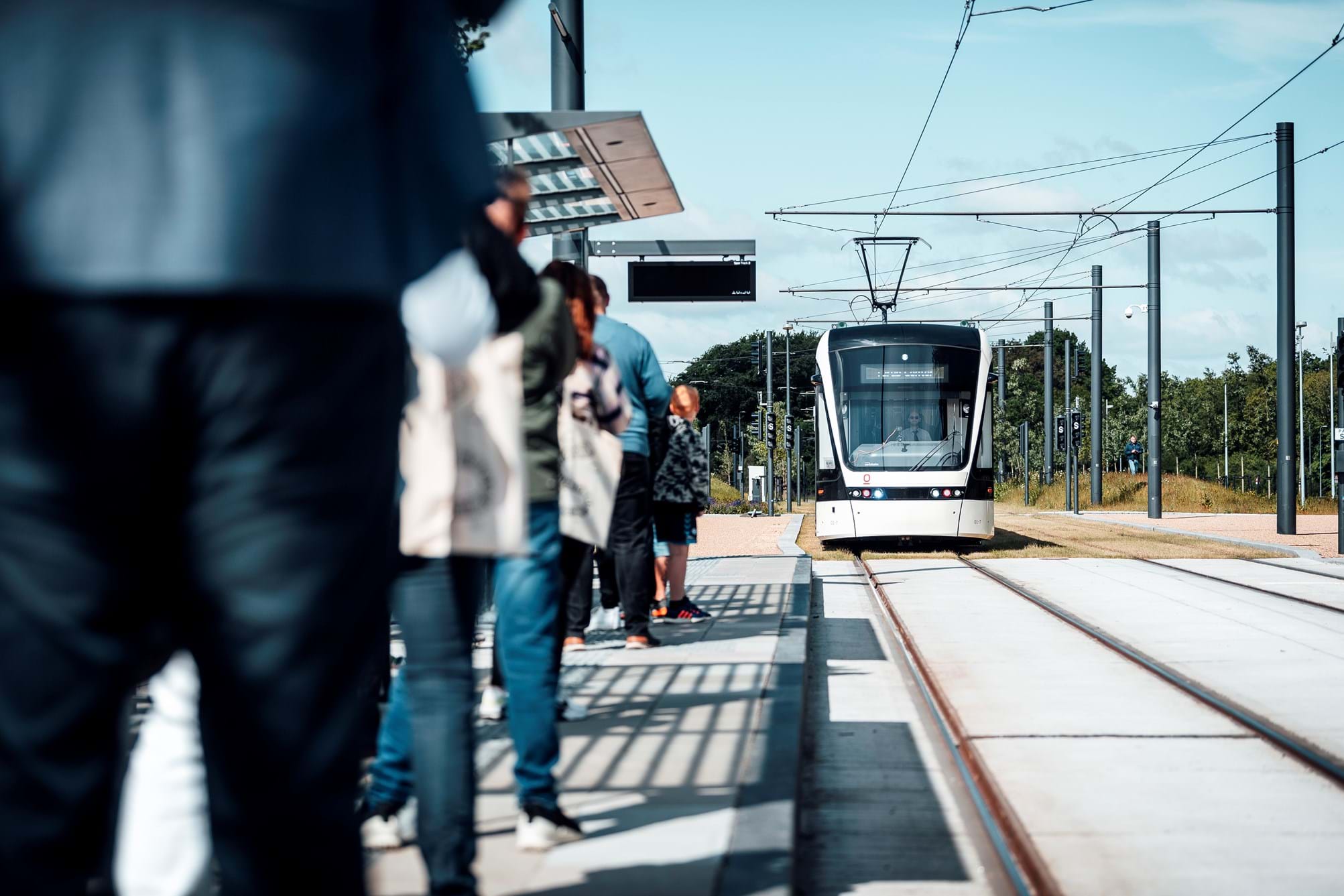 Ventede passagerer på perron og letbane i baggrunden